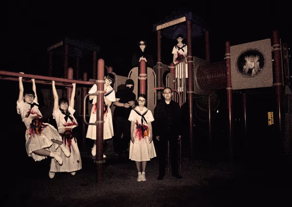 BiS y Hijokaidan en un tétrico parque de juegos infantiles, de noche; BiS jugando en el parque y usando vestidos blancos con el abdomen lleno de (aparentes) vísceras y sangre